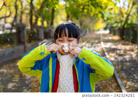 Asian little girl blowing nose with tissue in autumn park, cold and seasonal illness concept Asian little girl blowing nose with tissue in autumn park, cold and seasonal illness concept 142324281