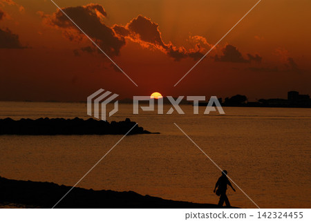 Silhouette of a person walking against the backdrop of a sunset over the sea Silhouette of a person walking against the backdrop of a sunset over the sea 142324455