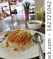 Thai crispy chicken rice dish served on a white plate with cucumber slices and broth 142325042