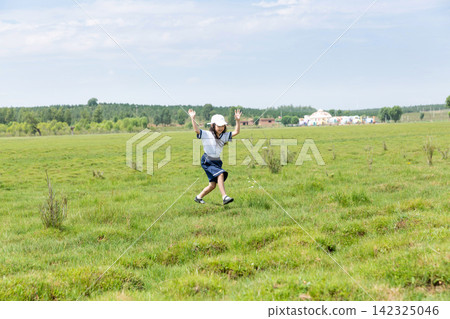 During the holiday, an energetic little Asian girl walks on a vast green lawn. 142325046