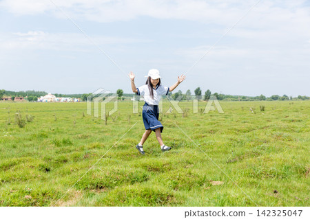 During the holiday, an energetic little Asian girl walks on a vast green lawn. 142325047