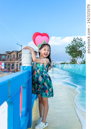 Cute little girl posing playfully on a colorful pedestrian walkway next to the ocean. Cute little girl posing playfully on a colorful pedestrian walkway next to the ocean. 142325076