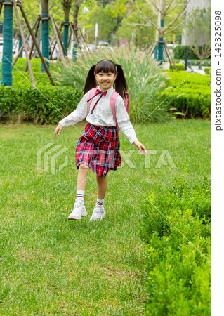 Asian elementary school students carrying their schoolbags happily walk in the city park after school. Asian elementary school students carrying their schoolbags happily walk in the city park after school. 142325098