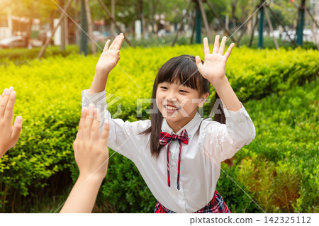 A happy young schoolgirl smiling and giving a high five to her friend outdoors during recess. A happy young schoolgirl smiling and giving a high five to her friend outdoors during recess. 142325112