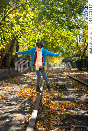 A joyful child standing on an autumn railway track with arms wide open under beautiful green and yellow trees. 142325117
