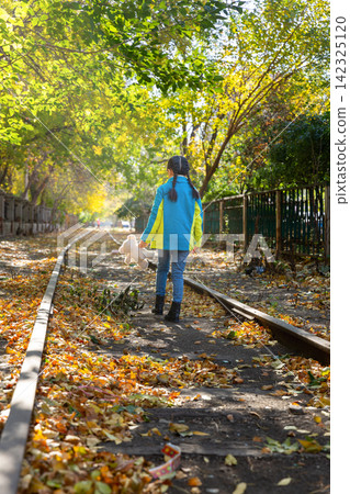 Back view of a child walking down a historic train track carrying a white teddy bear in autumn. Back view of a child walking down a historic train track carrying a white teddy bear in autumn. 142325120