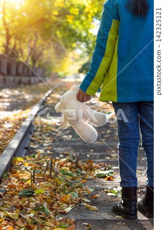 Back view of a child walking down a historic train track carrying a white teddy bear in autumn. Back view of a child walking down a historic train track carrying a white teddy bear in autumn. 142325121
