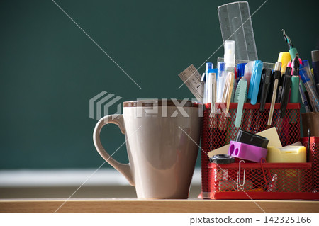 Stationery Holder with Assorted Pens and Rulers Next to Coffee Mug on Desk in Classroom 142325166