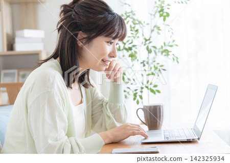 A woman smiling while using her computer in her living room at home. A woman smiling while using her computer in her living room at home. 142325934