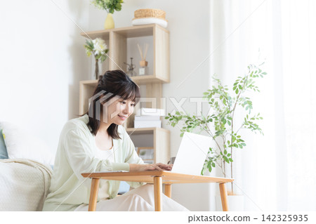 A woman smiling while using her computer in her living room at home. A woman smiling while using her computer in her living room at home. 142325935
