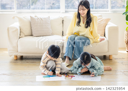 A mother watches over her children as they draw pictures in the living room. A mother watches over her children as they draw pictures in the living room. 142325954