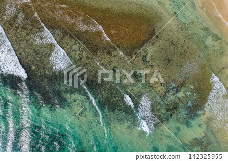 Aerial downward view of ocean waves crashing over the rugged rocky coastline at Brooms Head, capturing white surf, exposed rock formations and surrounding Pacific Ocean along the Clarence Valley coast Aerial downward view of ocean waves crashing over the rugged rocky coastline at Brooms Head, capturing white surf, exposed rock formations and surrounding Pacific Ocean along the Clarence Valley coast 142325955