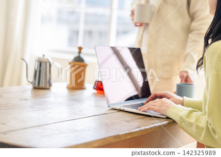 A woman operating a laptop and a man offering her a drink. A woman operating a laptop and a man offering her a drink. 142325989