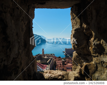 Dubrovnik, Croatia: The old town's bell tower and harbor as seen through the loopholes in the city walls. Dubrovnik, Croatia: The old town's bell tower and harbor as seen through the loopholes in the city walls. 142326808
