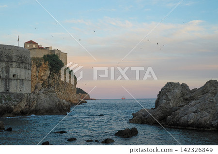 Dubrovnik Old Town: A sunset over a bay with cliffside fortresses and sailing ships, Croatia Dubrovnik Old Town: A sunset over a bay with cliffside fortresses and sailing ships, Croatia 142326849