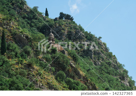 A small church and cross on a green mountaintop near Kotor, Montenegro. A small church and cross on a green mountaintop near Kotor, Montenegro. 142327365