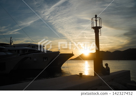 A yacht moored in the harbor of Korčula, Croatia, with silhouettes of people standing against the sunset. A yacht moored in the harbor of Korčula, Croatia, with silhouettes of people standing against the sunset. 142327452