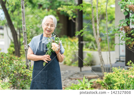 A senior woman with gray hair enjoying gardening in the yard of her home. 142327808