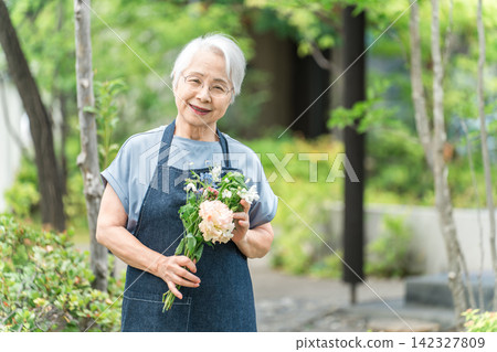 一位頭髮花白的老婦人在自家院子裡享受園藝的樂趣。 一位頭髮花白的老婦人在自家院子裡享受園藝的樂趣。 142327809