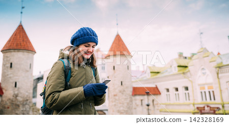 Tallinn, Estonia. Young Caucasian Woman Backpacker Tourist Enjoying Life, Smiling And Using Smartphone Near Landmark Viru Gate. Vacation In Old Town. Girl Surfing Net Internet In Phone Tallinn, Estonia. Young Caucasian Woman Backpacker Tourist Enjoying Life, Smiling And Using Smartphone Near Landmark Viru Gate. Vacation In Old Town. Girl Surfing Net Internet In Phone 142328169