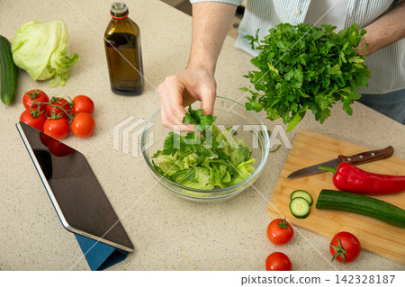 Cooking. Person adds fresh parsley to bowl of salad ingredients in stylish kitchen Cooking. Person adds fresh parsley to bowl of salad ingredients in stylish kitchen 142328187