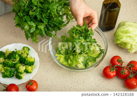 Cooking. Cook combines fresh lettuce and parsley in a salad bowl Cooking. Cook combines fresh lettuce and parsley in a salad bowl 142328188