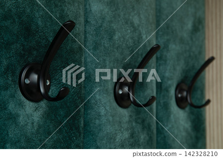Wall hooks are featured prominently on a textured green backdrop Wall hooks are featured prominently on a textured green backdrop 142328210