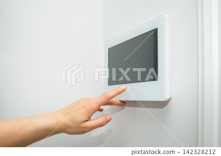 Hand interacts with touchscreen control panel mounted on wall 142328212