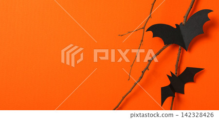 Halloween. Black paper bats hang on branches against an orange backdrop Halloween. Black paper bats hang on branches against an orange backdrop 142328426