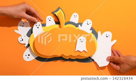 Halloween. Hands assemble colorful Halloween decorations featuring pumpkins and ghosts Halloween. Hands assemble colorful Halloween decorations featuring pumpkins and ghosts 142328434