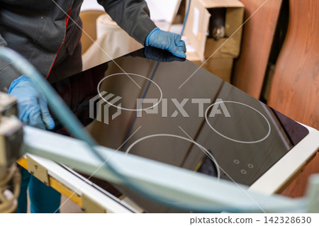 Worker installing black glass induction cooktop in kitchen setting Worker installing black glass induction cooktop in kitchen setting 142328630