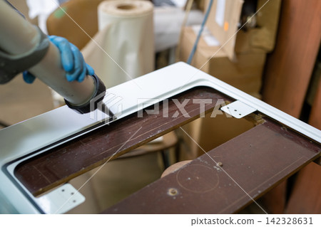 Hand applying sealant to white frame edge in workshop 142328631