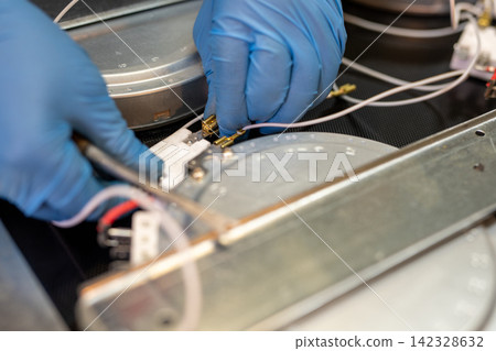 Closeup of gloved hands connecting wires to metal component in technical device Closeup of gloved hands connecting wires to metal component in technical device 142328632