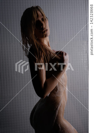 Woman showering with wet hair and soap suds against tiled wall 142328668