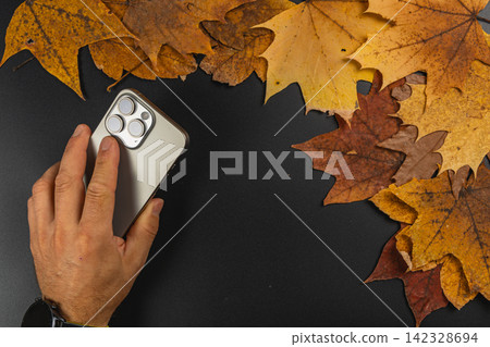 Smartphone on a black surface surrounded by autumn leaves 142328694