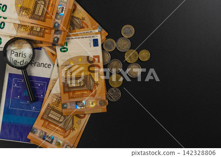 Banknotes and coins with a magnifying glass on a black surface Banknotes and coins with a magnifying glass on a black surface 142328806