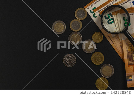Examining euro banknotes and coins with a magnifying glass Examining euro banknotes and coins with a magnifying glass 142328848