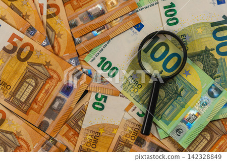 Examining euro banknotes with a magnifying glass for financial review Examining euro banknotes with a magnifying glass for financial review 142328849