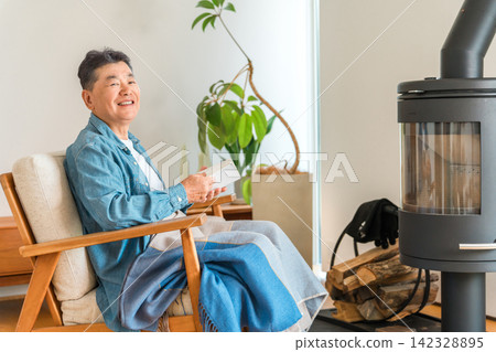 一位老人坐在客廳的燃木爐前的椅子上看書。 一位老人坐在客廳的燃木爐前的椅子上看書。 142328895
