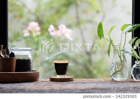 Coffee glass cup and roasted coffee beans on wooden table with flowers background Coffee glass cup and roasted coffee beans on wooden table with flowers background 142329383