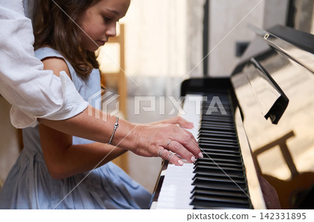 Piano teacher guiding young girl through a hands-on piano lesson in a warm home setting Piano teacher guiding young girl through a hands-on piano lesson in a warm home setting 142331895