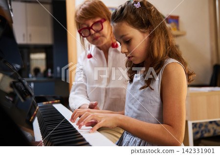 Young girl taking piano lesson with teacher at home piano class Young girl taking piano lesson with teacher at home piano class 142331901