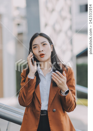 Young professional woman talking on phone and holding coffee outside modern office building Young professional woman talking on phone and holding coffee outside modern office building 142331954