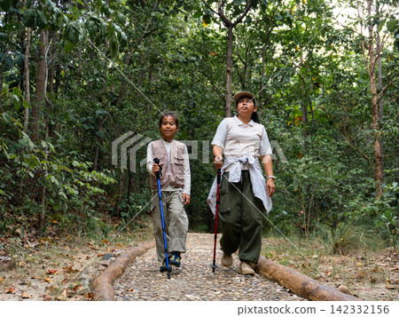 Asian mother and daughter walking with trekking poles on nature trail in forest Asian mother and daughter walking with trekking poles on nature trail in forest 142332156