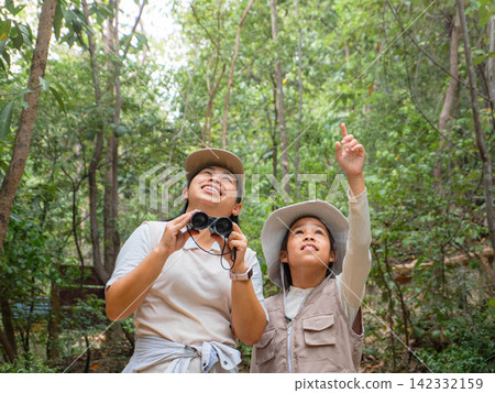 Asian mother and daughter birdwatching in forest with girl pointing up at treetops Asian mother and daughter birdwatching in forest with girl pointing up at treetops 142332159