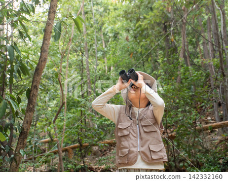 Little Asian girl wearing safari hat and vest looking through binoculars on forest nature trail Little Asian girl wearing safari hat and vest looking through binoculars on forest nature trail 142332160