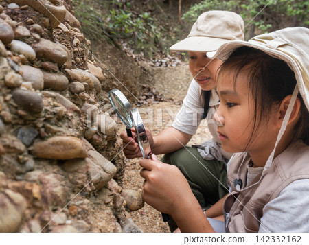 Asian mother and daughter looking through magnifying glass at geological rock stratum Asian mother and daughter looking through magnifying glass at geological rock stratum 142332162