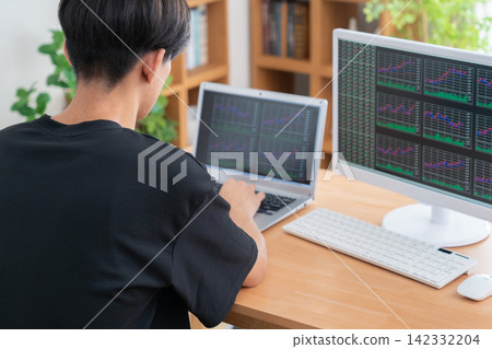 A young man invests in stocks from home. A young man invests in stocks from home. 142332204
