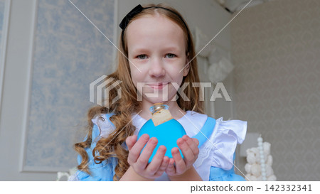 Young Girl Holding Blue Heart Gift Box Inside. Child With Curly Hair And Headband In Pastel Decorated Room. Cheerful Young Girl Dons Ruffled Blue Dress And Smiles Warmly Inside Cozy Pastel Setting Young Girl Holding Blue Heart Gift Box Inside. Child With Curly Hair And Headband In Pastel Decorated Room. Cheerful Young Girl Dons Ruffled Blue Dress And Smiles Warmly Inside Cozy Pastel Setting 142332341