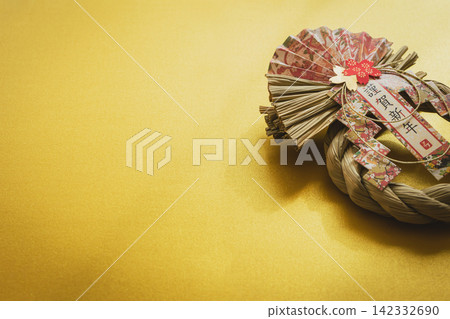新年裝飾品,以金色為背景,繫著一條寫有「新年快樂」字樣的注連繩。 新年裝飾品,以金色為背景,繫著一條寫有「新年快樂」字樣的注連繩。 142332690